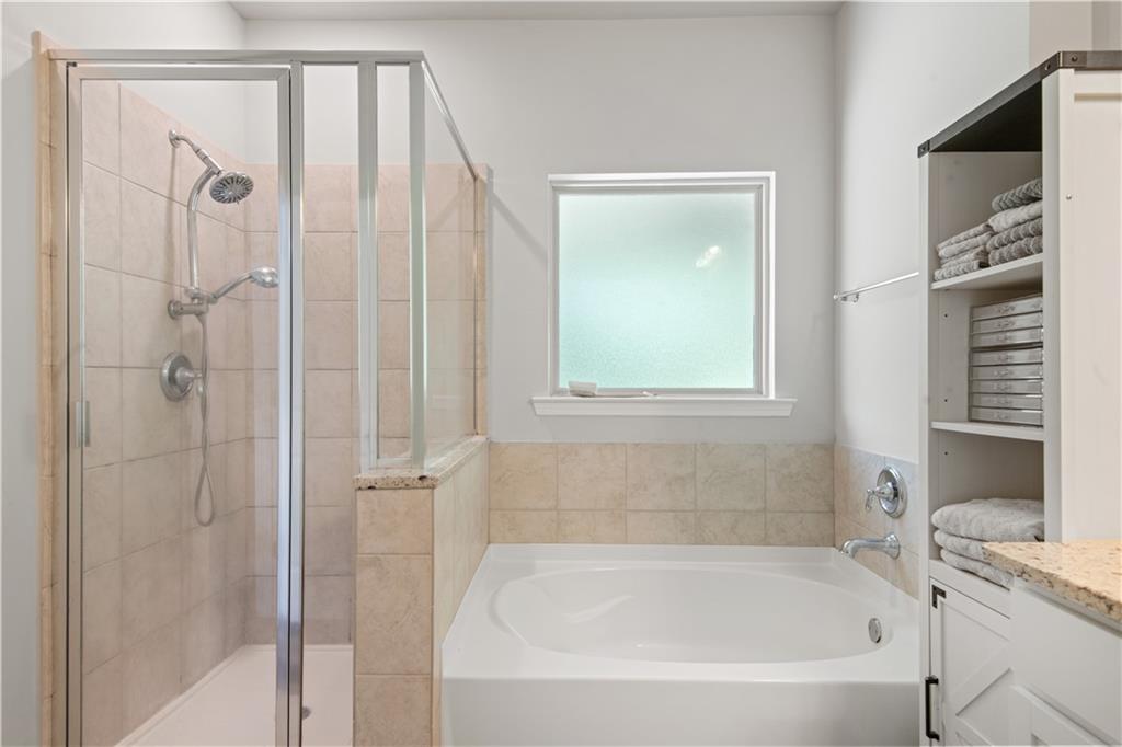 Bathroom with a glass-enclosed shower, soaking tub, frosted window, and built-in towel shelving.