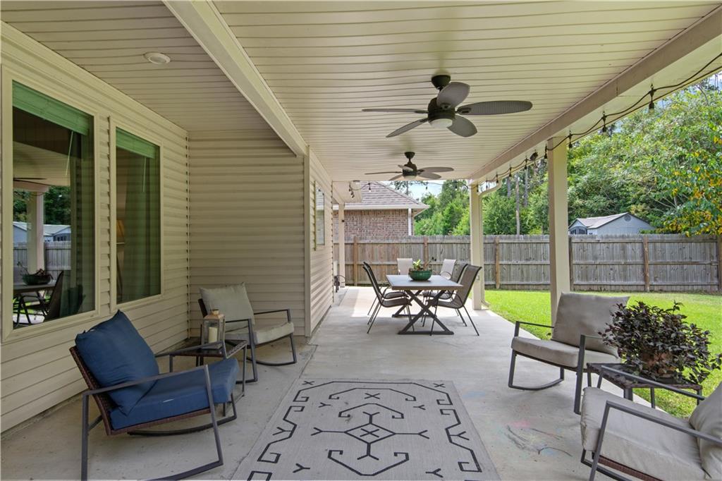 Covered patio with ceiling fans, lounge seating, a dining set, and a fenced backyard.