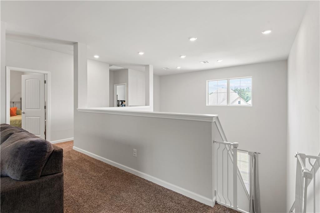 Upstairs sitting area with a dark sofa, carpeted floor, and railing overlooking the stairwell.
