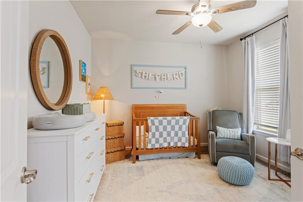 Nursery with a wooden crib, white dresser, and gray rocking chair beside a large window.