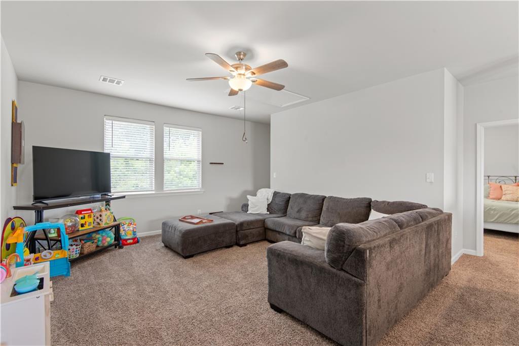 Living room with a gray sectional sofa, ceiling fan, and television beside two windows.