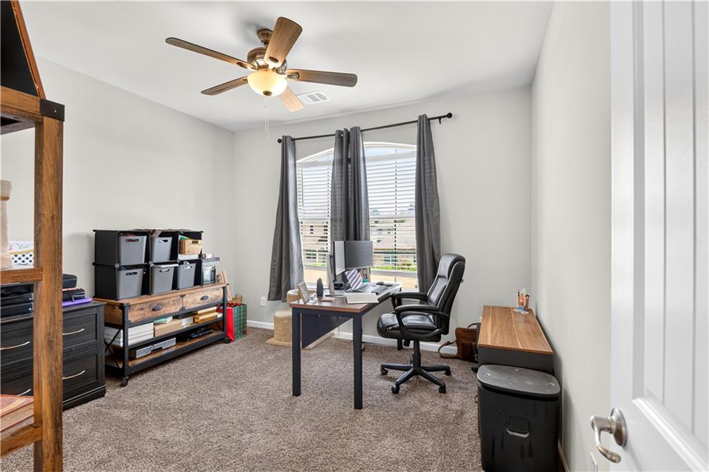 Furnished home office with a desk, black chair, and curtained window.