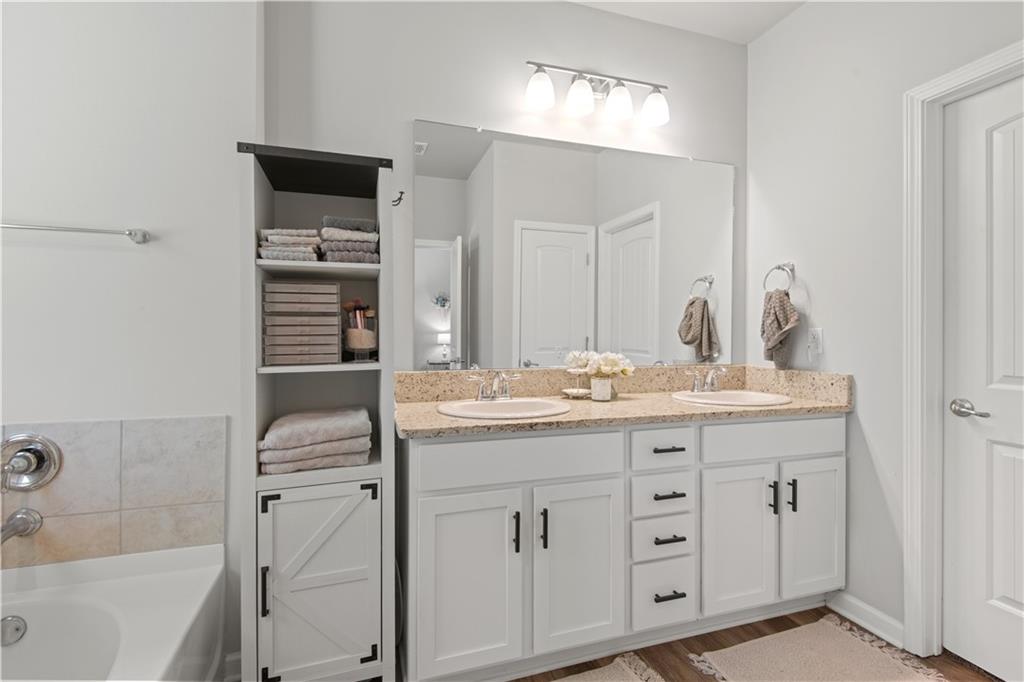 Bathroom with a double-sink vanity, beige stone countertop, and open shelving stocked with towels.