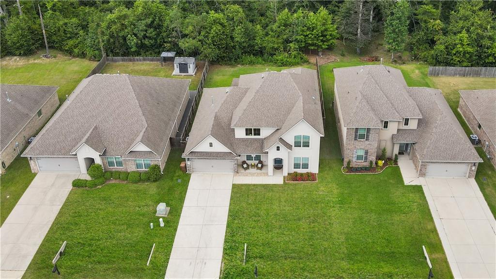 Aerial view of a white home with a front porch, driveway, and tree-lined backyard.