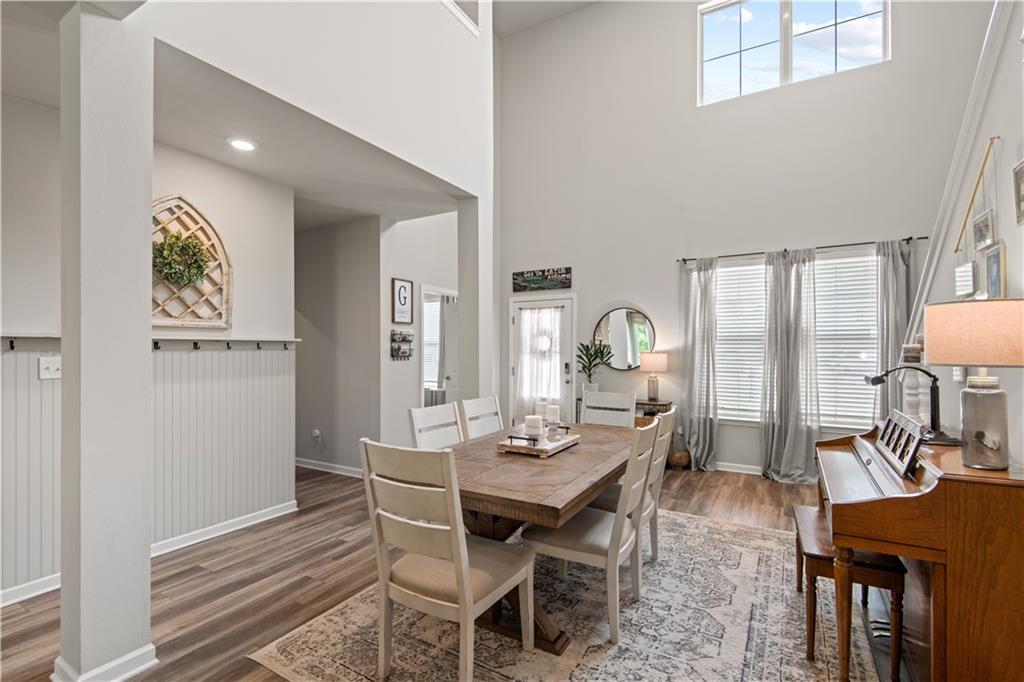 Dining room with a wooden table, white chairs, high ceilings, and a piano.