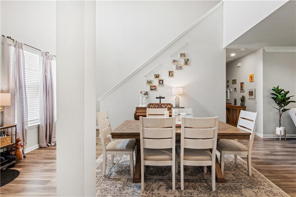 Dining room with a wood table, upholstered chairs, piano, and photos displayed along the staircase.