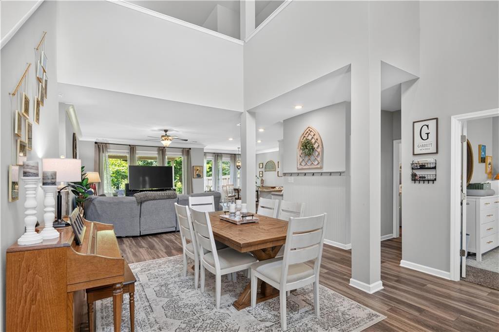 Open dining area with a wood table and white chairs beside a high-ceilinged living room.