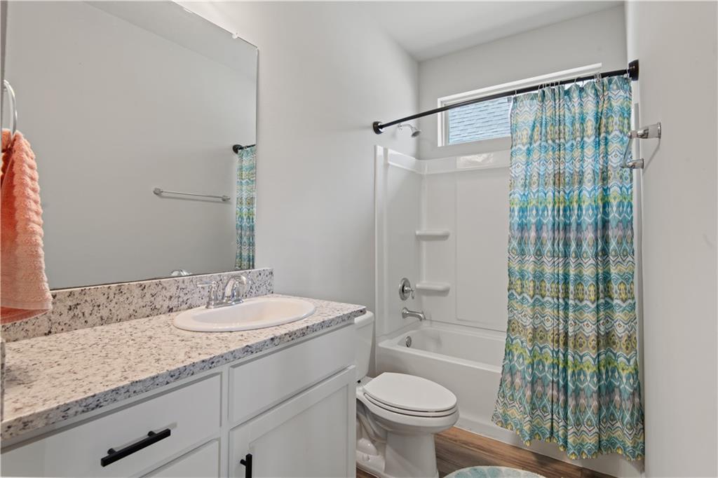 Bathroom with a speckled stone vanity, white tub and blue-green patterned shower curtain.