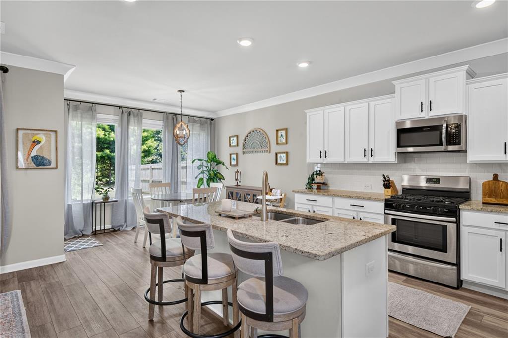 Kitchen with a granite island and bar stools, white cabinetry, stainless steel appliances, and an adjoining dining area.