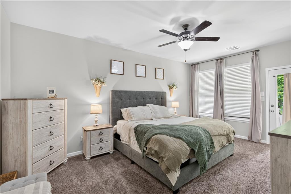 Bedroom with a gray upholstered bed, green throw, matching dressers, and tall curtained windows.