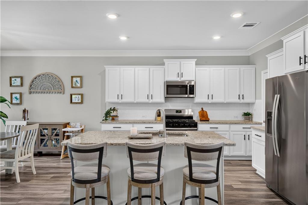 Kitchen with white cabinets, stainless steel appliances, and a stone island with three bar stools.