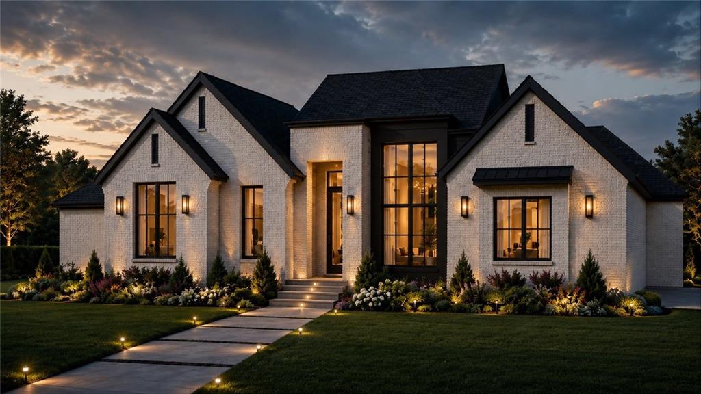 White-brick home with tall illuminated windows, landscaped gardens, and a walkway at dusk.