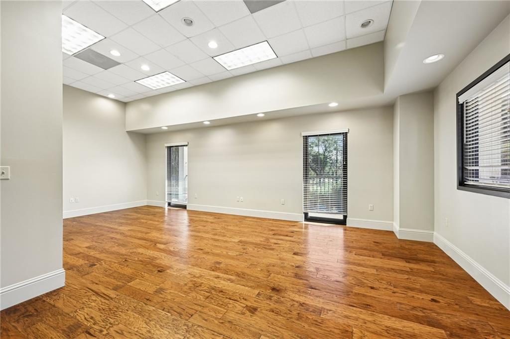 Empty room with hardwood floors, pale walls, and windows with blinds.