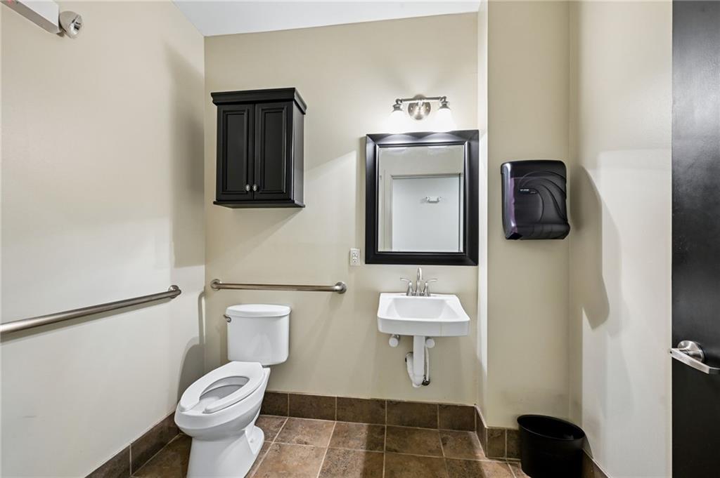 Bathroom with stainless steel grab bars, a wall-mounted sink, and brown tile flooring.