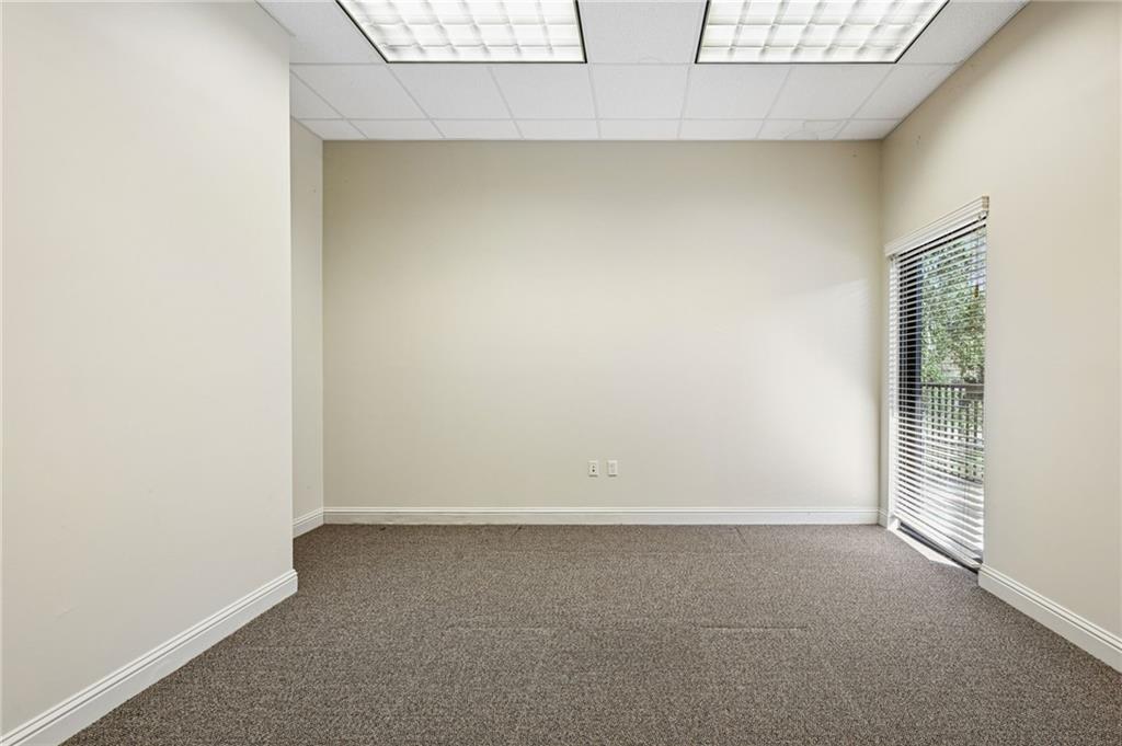 Vacant carpeted room with fluorescent ceiling panels and a glass door with blinds.