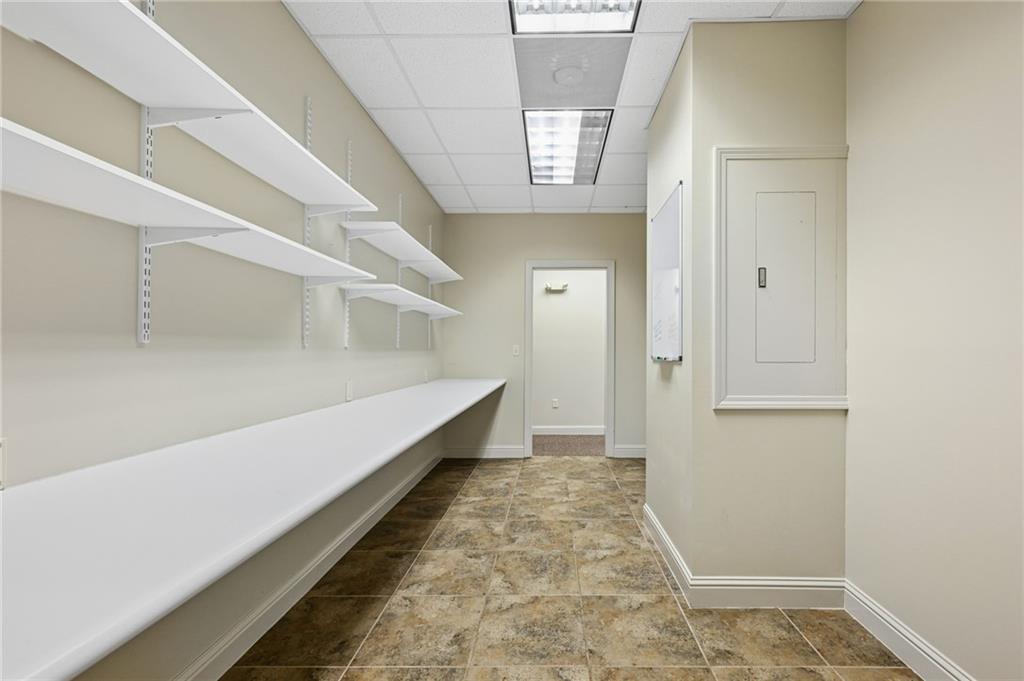 Empty workroom with long white counters, wall shelves, and a mottled tile floor.