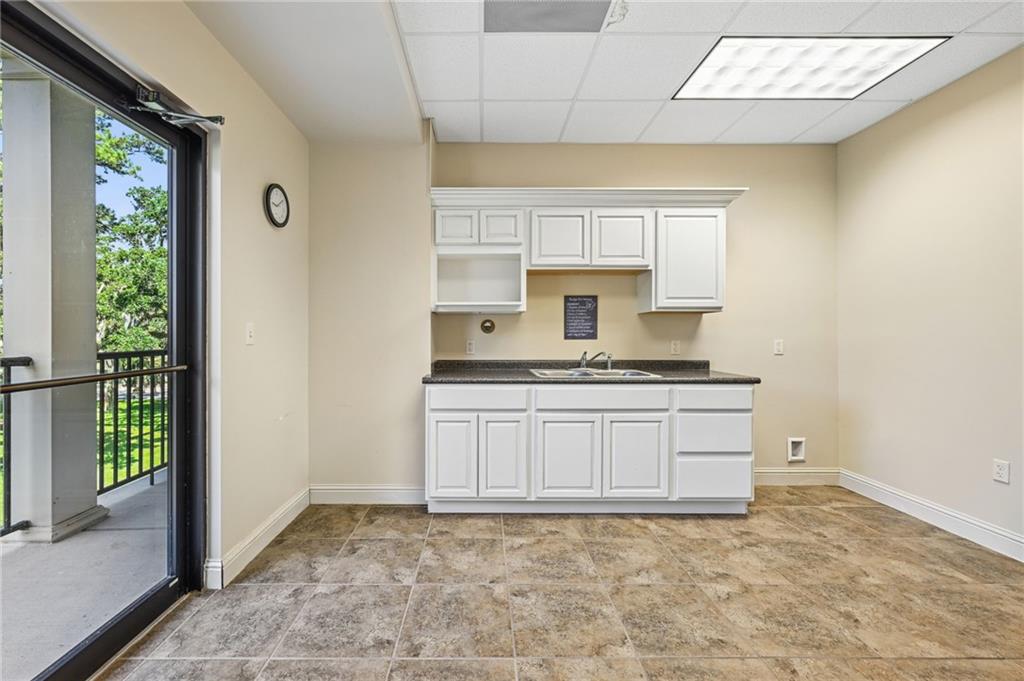Empty kitchenette with white cabinets and a sink beside a glass door opening to a balcony.