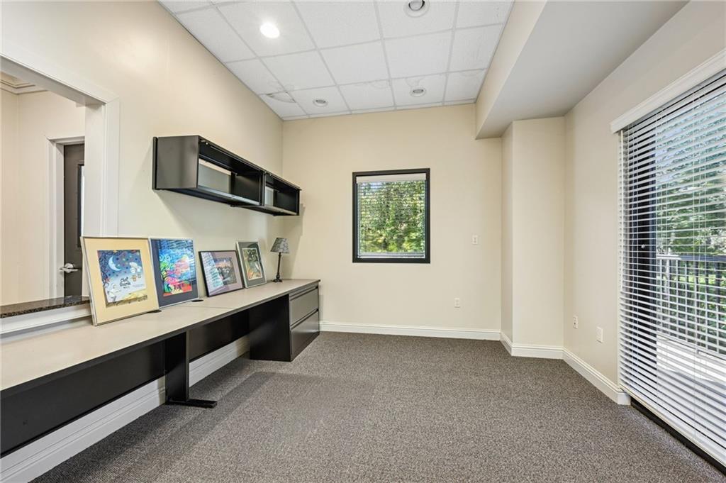 Office with a long built-in desk, framed artwork, and windows overlooking greenery.