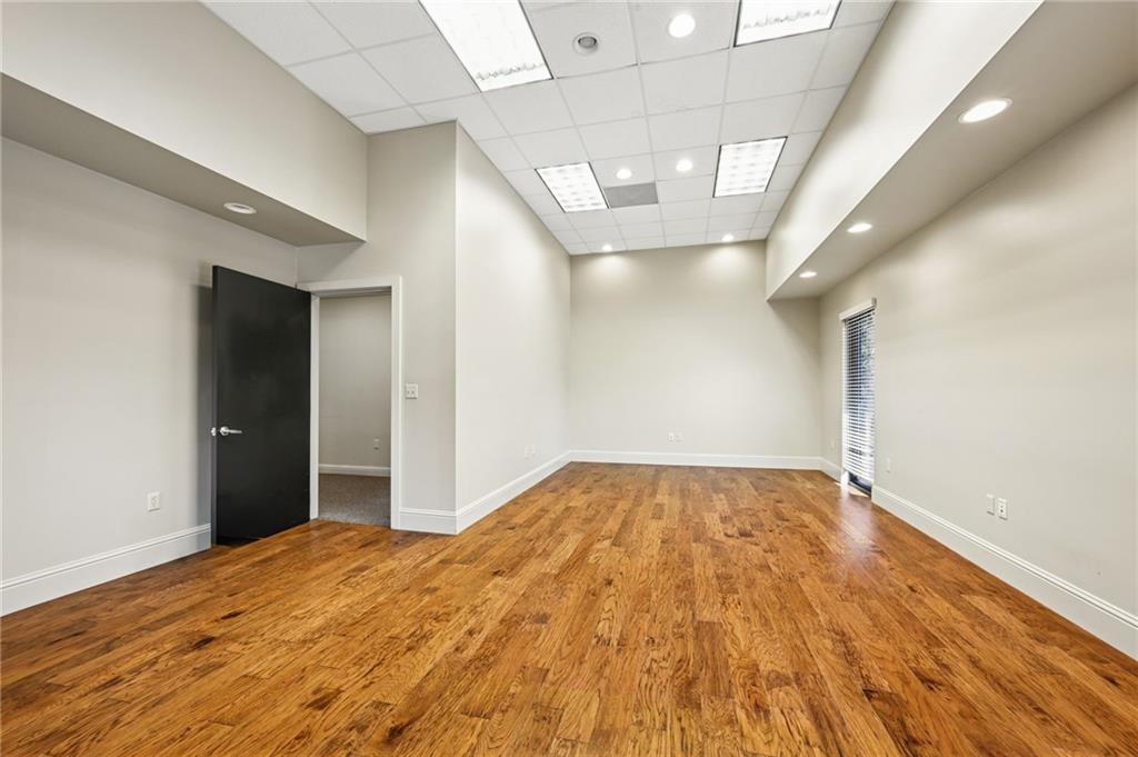 Empty interior room with hardwood floors, a suspended ceiling, and an open dark door.