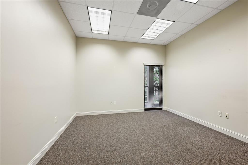 Empty office with brown carpet, fluorescent ceiling lights, and a narrow window with blinds.