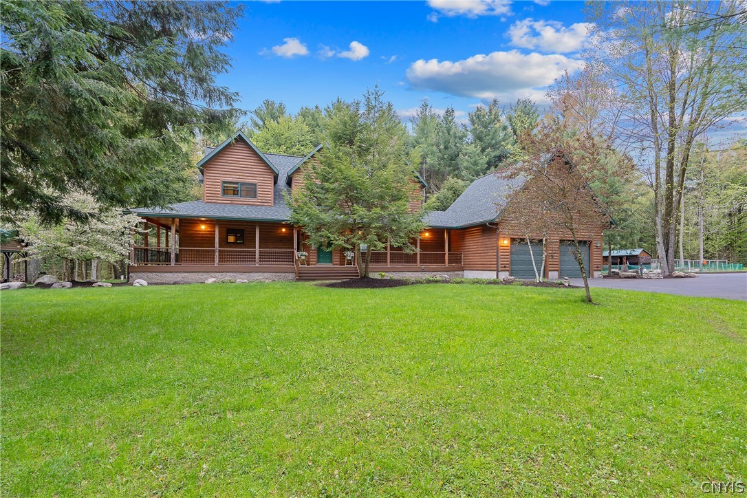 Log-style home with a covered porch and attached garage, set among mature trees behind a broad lawn.