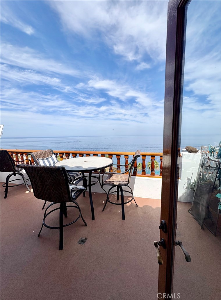 Furnished balcony overlooking the ocean, with a round table and wicker chairs beside a wooden railing.