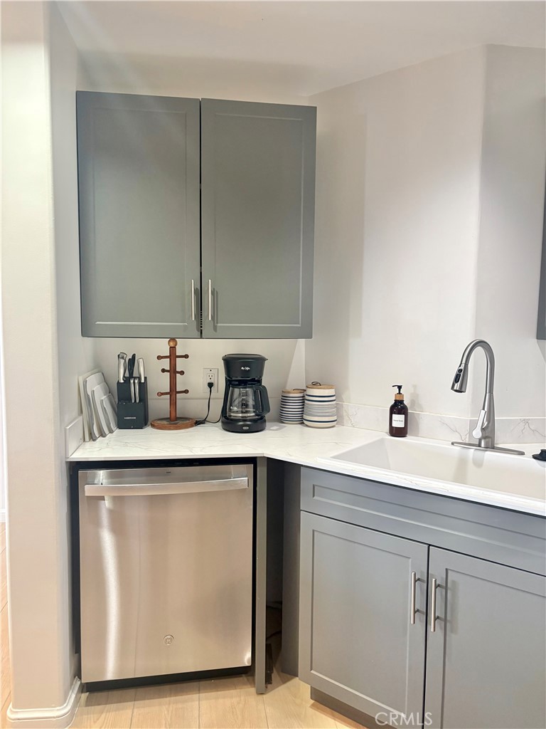 Kitchen corner with gray cabinets, a stainless steel dishwasher, and a white sink beneath a tall faucet.