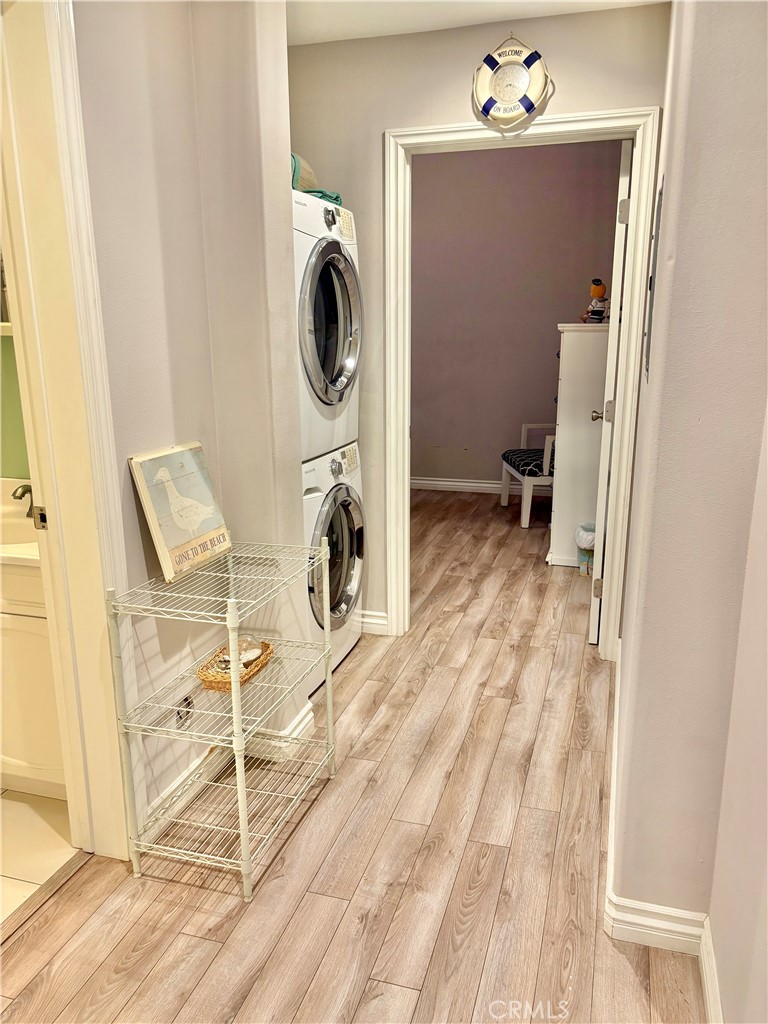 Laundry area with stacked washer and dryer, wood-look flooring, and a doorway to a small room.