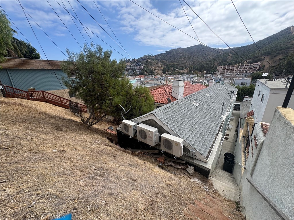 Hillside house with a gray shingle roof and three outdoor AC units, overlooking Avalon homes and hills.