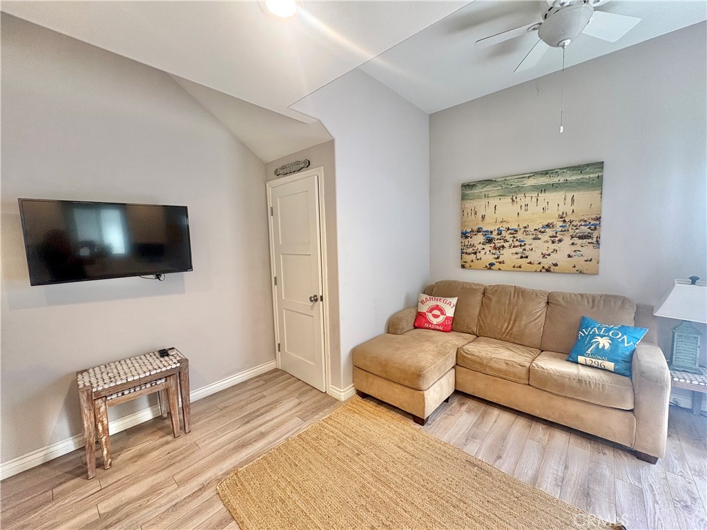 Living room with beige sectional, beach artwork, wall-mounted television, and light wood-look flooring.