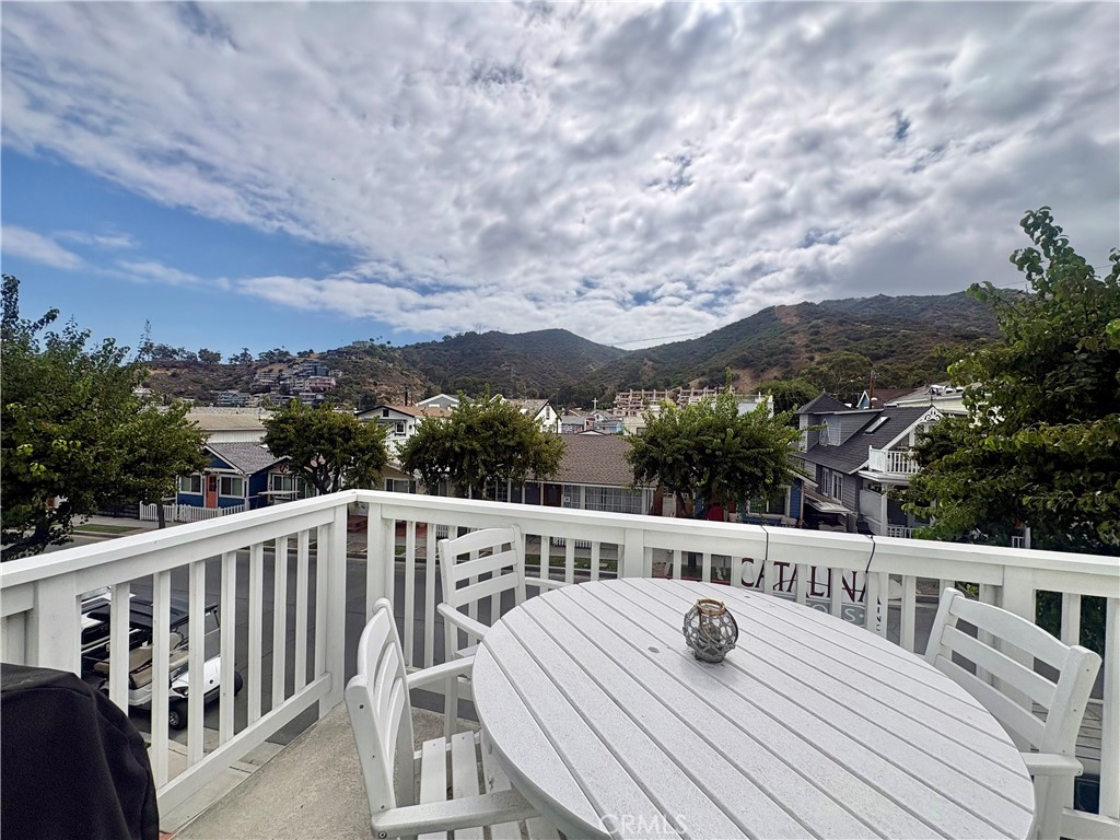 Furnished balcony with white dining set overlooking neighborhood homes and green hills.