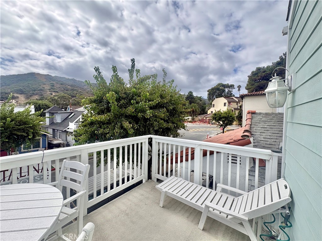 Elevated deck with white patio furniture overlooking rooftops, trees, and a green hillside.