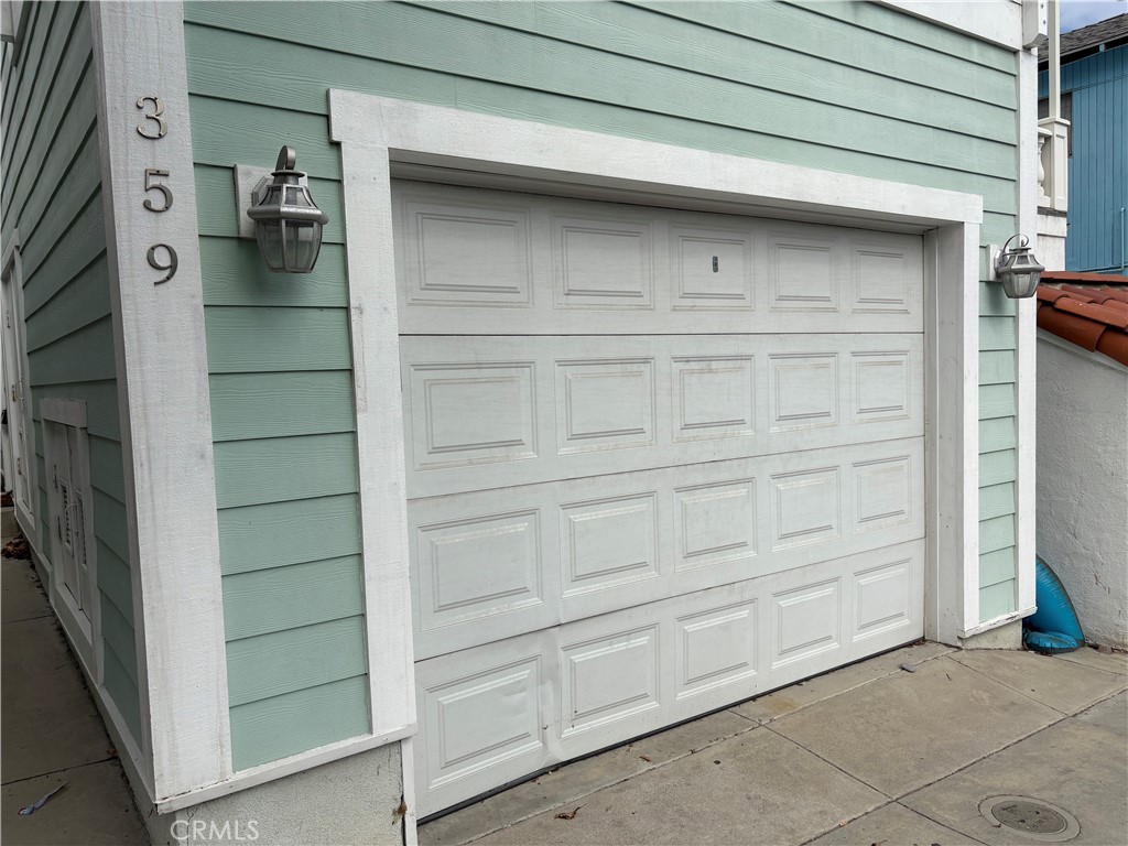 White paneled garage door framed by seafoam-green siding and wall lanterns.