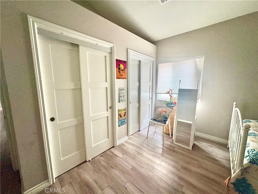 Bedroom with white sliding closet doors, wood-look flooring, a chair, and a full-length mirror.
