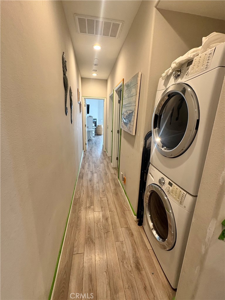 Hallway laundry area with stacked front-loading washer and dryer and wood-look flooring.