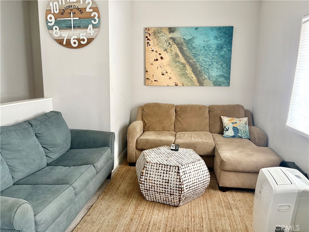 Living room with tan chaise sectional, blue-gray sofa, patterned ottoman, and aerial beach artwork.