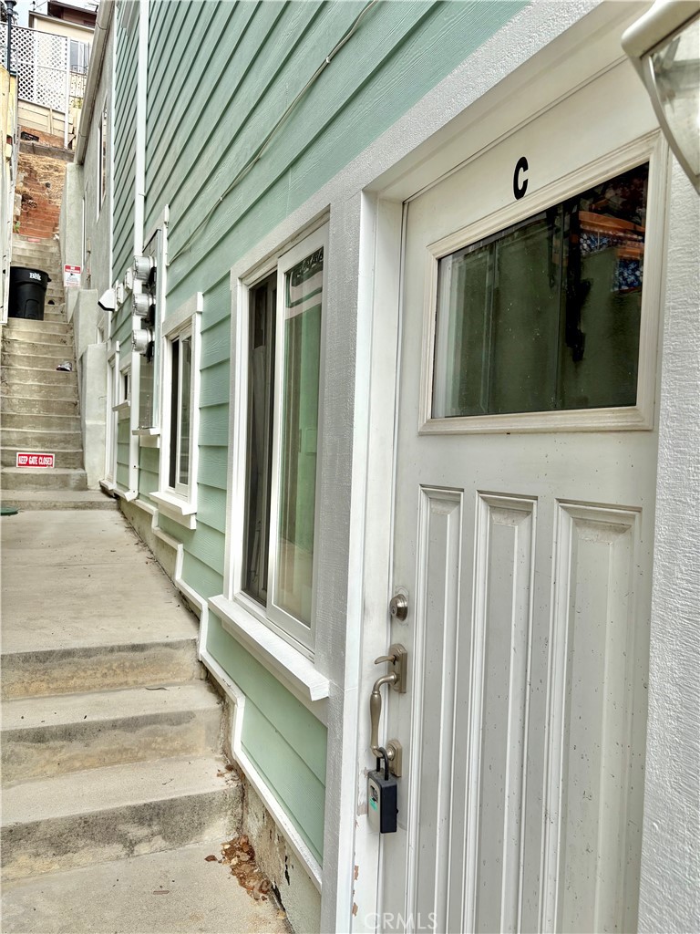White entry door marked C beside mint-green siding, with concrete steps along the building.