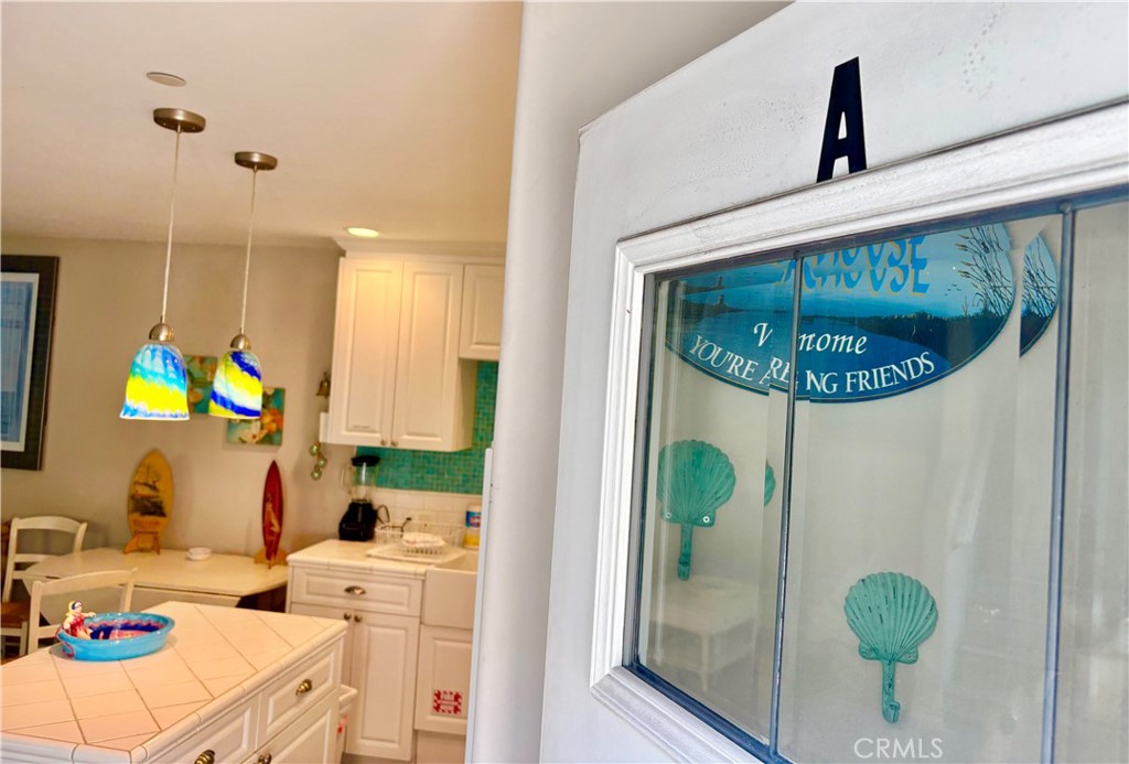 White kitchen with a tiled island, turquoise backsplash, and colorful pendant lights beside a shell-decorated glass door.