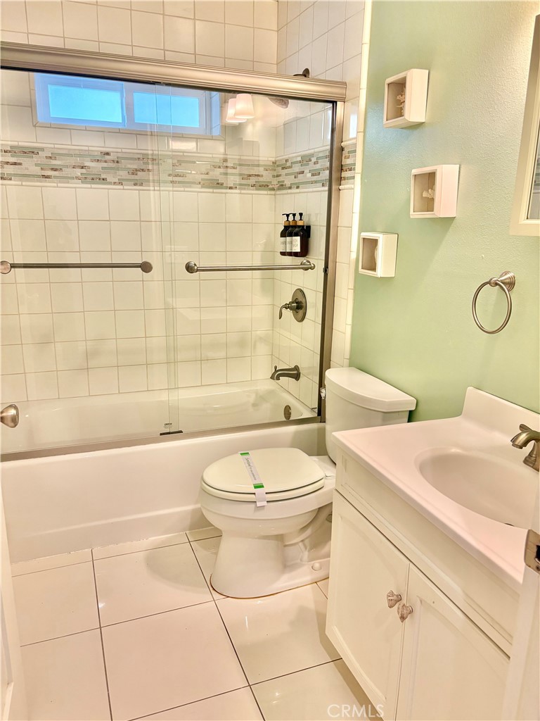 Bathroom with glass-enclosed tub, tiled walls, toilet, and white vanity against a pale green wall.