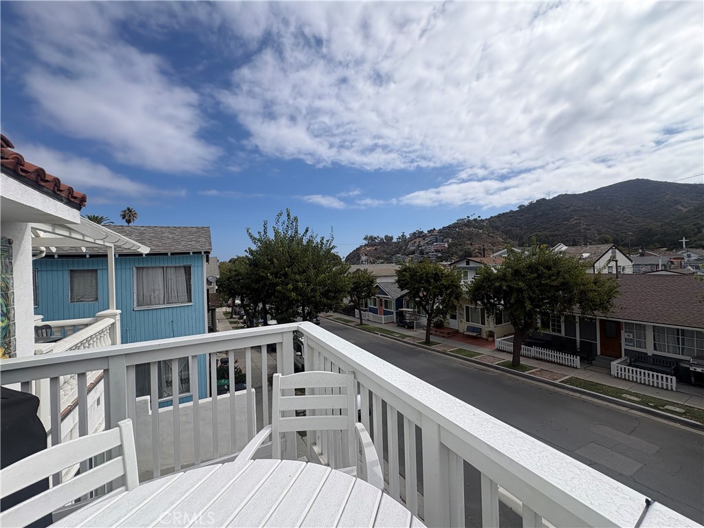 Balcony overlooking a residential street and hillside, with a white patio table and chairs.