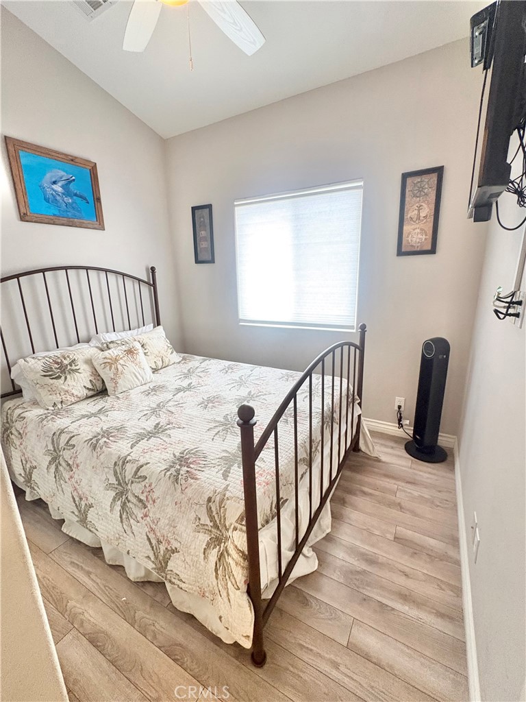 Bedroom with a dark metal bed, floral quilt, wood-look flooring, and bright window.
