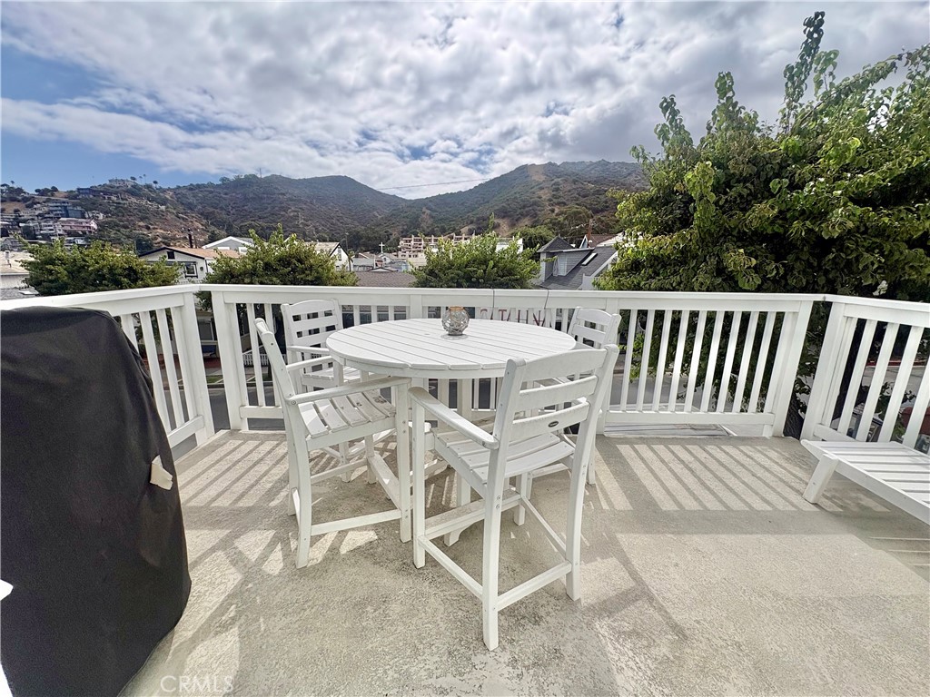 Outdoor deck with white dining set and views of green hills beyond the railing.