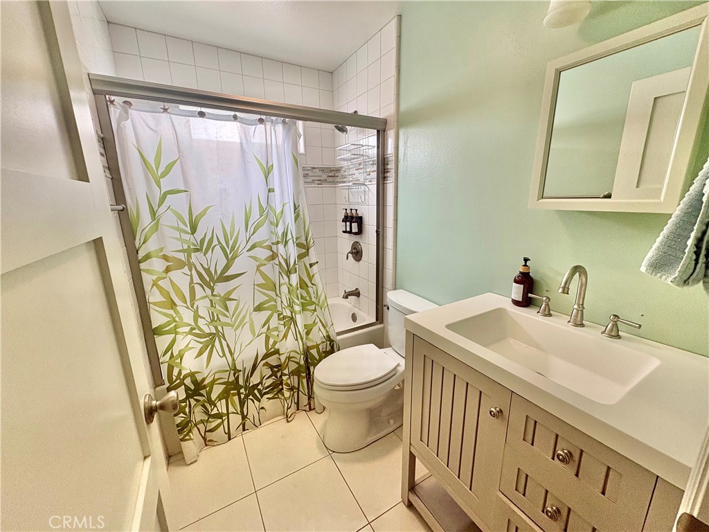 Bathroom with a white vanity, toilet, and tiled shower behind a bamboo-patterned curtain.