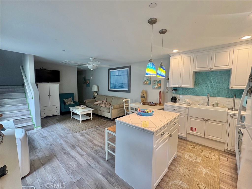 Open-plan kitchen and living room with a white island, teal tile backsplash, and beige sofa.
