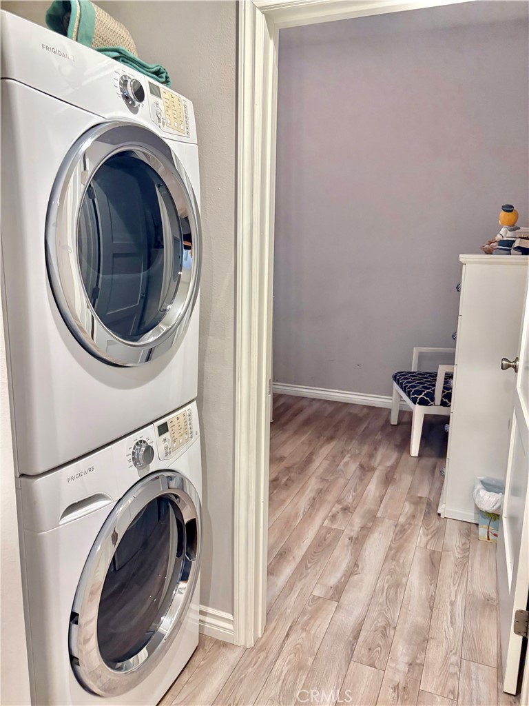 Stacked Frigidaire washer and dryer beside a doorway to a room with wood-look flooring and a small bench.