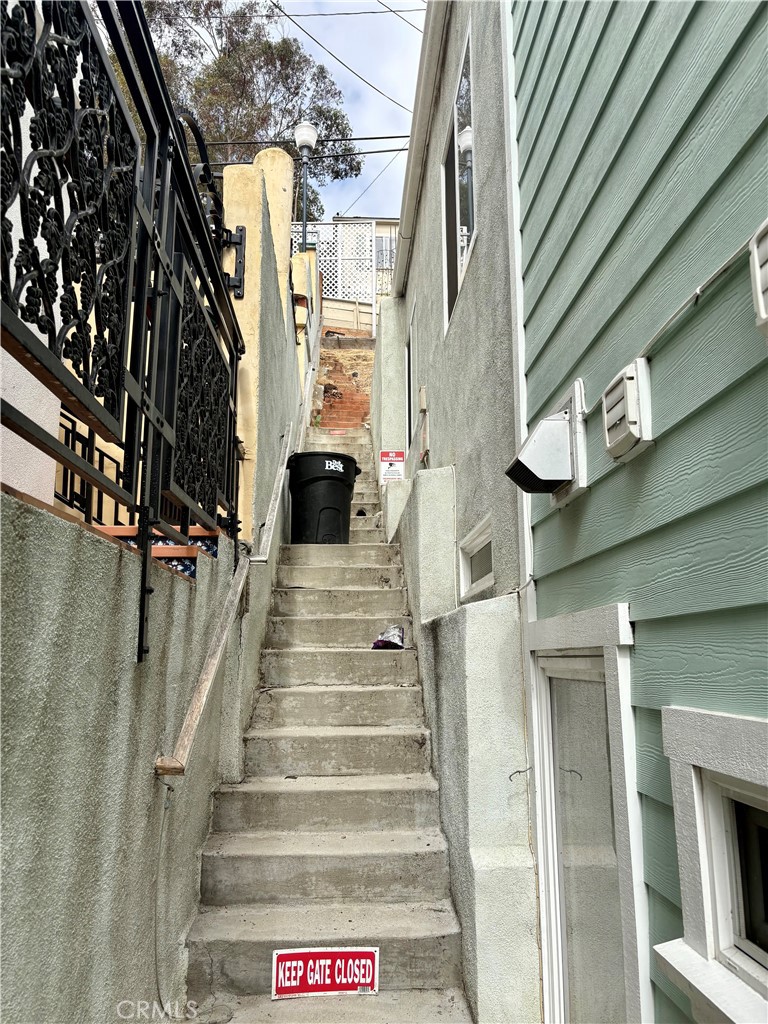 Exterior concrete stairs between buildings, beside a black wrought-iron gate and pale green siding.