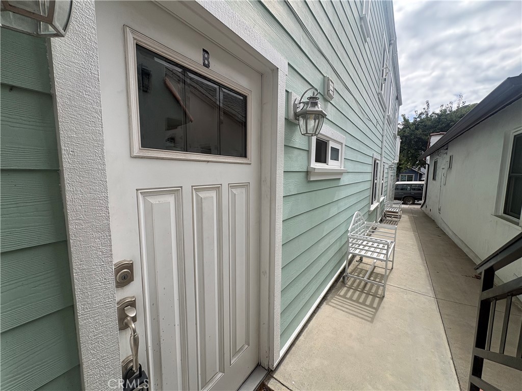 Side entrance with a white door marked B beside mint-green siding and a narrow walkway with white chairs.