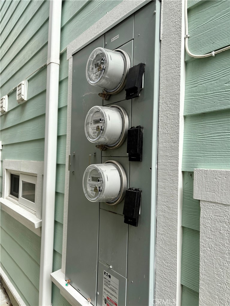 Three electric meters on mint-green house siding beside a white downspout.