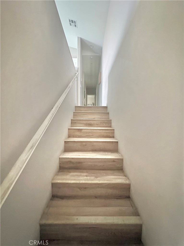 Narrow light-wood staircase with a white handrail leading to a bright upper landing.