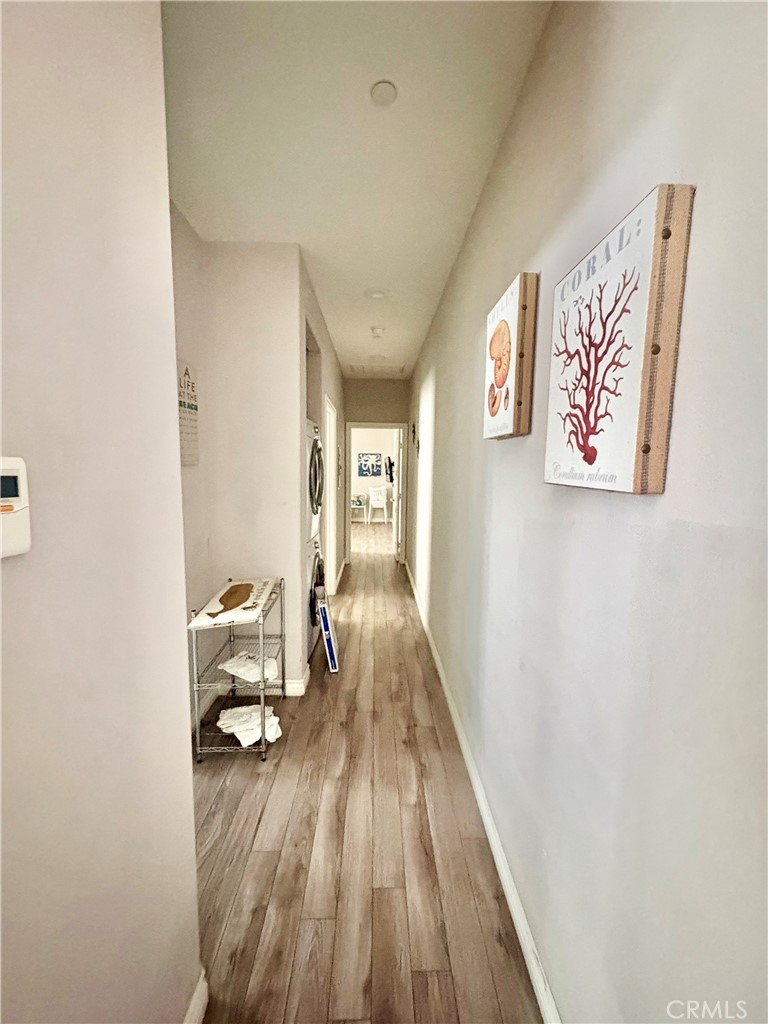 Long hallway with wood-look flooring, framed coral artwork, and a small metal console table.